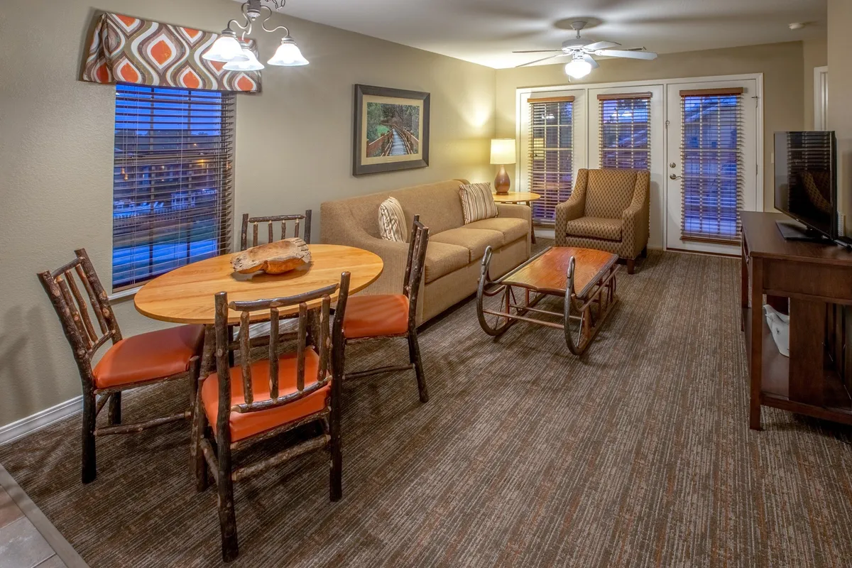 A harmonious open-plan area where a dining table, soft sofa, and armchair create natural zones for both relaxing and sharing meals. The space is filled with welcoming light, and the layout seamlessly connects lounging and dining, embodying a communal atmosphere that encourages mingling and shared experiences.