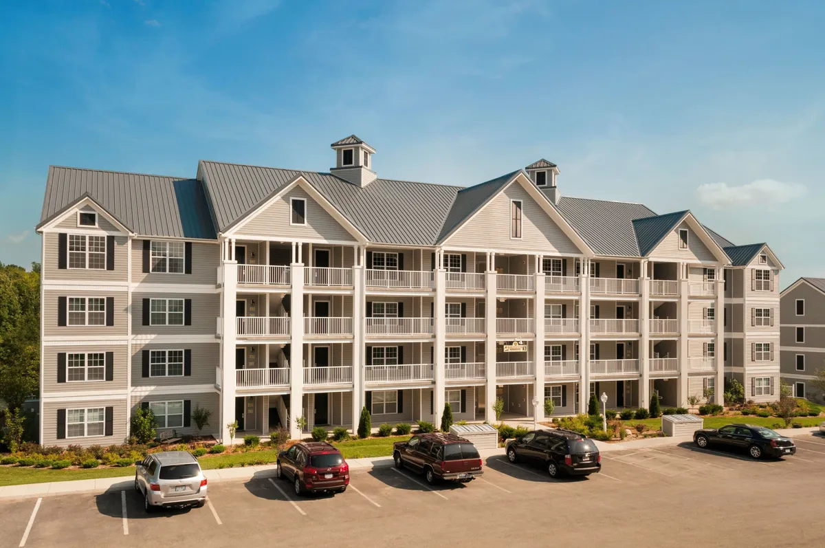 This exterior image features modern resort architecture with multiple balconies overlooking landscaped gardens and a parking lot. The inviting scene shows residents relaxing on their balconies and gathering outdoors, suggesting a vibrant and social resort atmosphere.