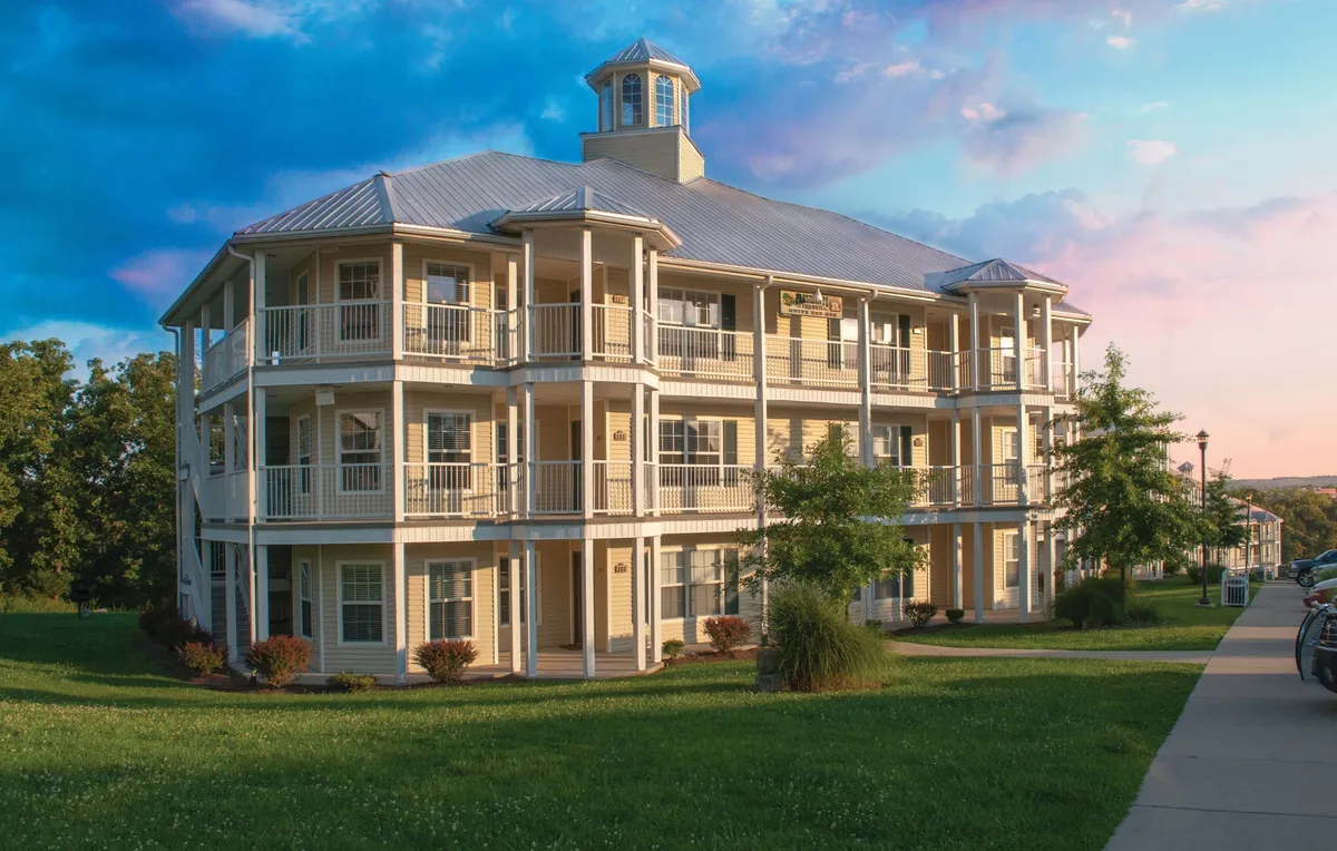 The exterior of the resort building is framed by a vibrant sky and well-maintained green spaces. Balconies add architectural interest and create spaces for guests to enjoy the outdoors, while the surrounding trees and lawn suggest ample space for play and relaxation. The scene feels both welcoming and dynamic, hinting at the range of activities available nearby.