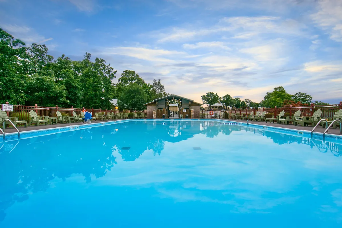 This image showcases a sparkling swimming pool surrounded by lush greenery, with several lounge chairs arranged poolside and a pavilion providing covered seating. The relaxed scene suggests opportunities for swimming, sunbathing, or enjoying group gatherings by the water. The ambiance is inviting, especially during sunset when the area is bathed in warm light.