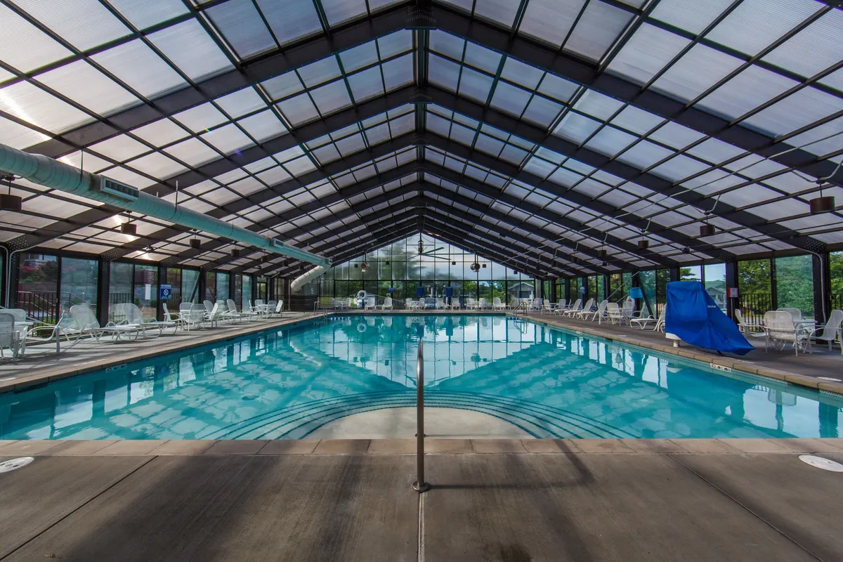 This image showcases a spacious indoor swimming pool area bathed in natural light from a glass roof. Sleek loungers line the pool, evoking a sense of tranquility and relaxation. The overall setting is modern, calming, and designed for unwinding after a busy day, whether swimming or lounging.